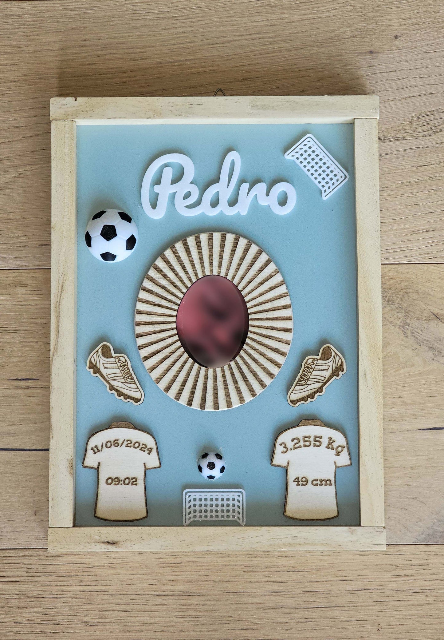 Quadretto che rappresenta elementi del gioco del calcio, come palloni, magliette e porte. Nelle magliette ci sono i dati di nascita del bambino per cui il quadretto è stato fatto.