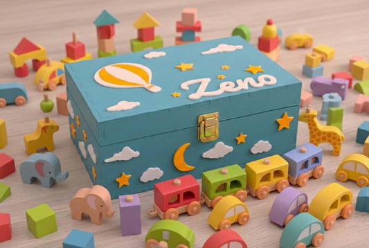 Scatola dei ricordi blu con elementi in pla biodegradabile rappresentanti stelle, nuovle ed una mongolfiera. La scatola è personalizzata con il nome del bambino