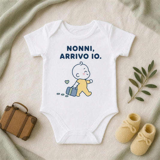 Body bianco con la frase «Nonni, arrivo io.» accanto a una valigetta in cuoio, scarpine gialle e un rametto d'ulivo