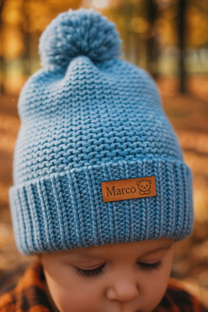 Mostra primo piano del berretto di lana fatto a mano da Bimbi Unici, con etichetta in cuoio personalizzata con il nome del bimbo e una icona.
