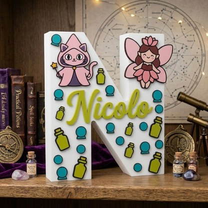 Lettera N decorativa 3D personalizzata con il nome Nicolo in rilievo verde. Design a tema magia e fantasy con illustrazioni di un gatto mago rosa, una fatina, boccette di pozioni e sfere di cristallo azzurre.