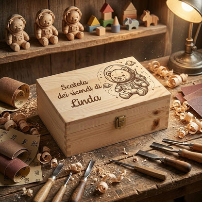 Scatola dei ricordi in legno personalizzata con incisione di un orsetto astronauta e la scritta "Scatola dei ricordi di Linda", con chiusura in metallo. Il cofanetto artigianale è appoggiato su un rustico banco da lavoro in legno, circondato da trucioli, rotoli di carta vetrata e sgorbie da intaglio. Sullo sfondo, una mensola con giocattoli in legno e una lampada da tavolo accesa.