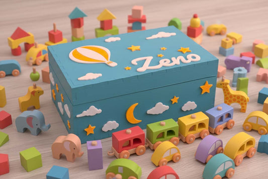 Scatola dei ricordi blu con elementi in pla biodegradabile rappresentanti stelle, nuovle ed una mongolfiera. La scatola è personalizzata con il nome del bambino