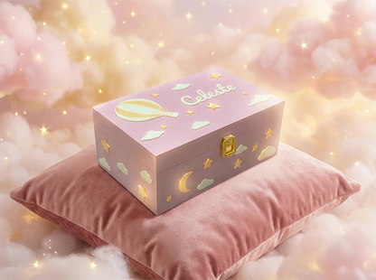 Scatola dei ricordi con nome "Celeste" personalizzato, di colore rosa, per bambina. Decorata con una mongolfiera circondata da nuvole e stelle. L'ambientazione è fantasy.