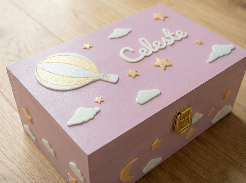 Scatola dei ricordi con nome personalizzato, di colore rosa, per bambina. Decorata con una mongolfiera circondata da nuvole e stelle.