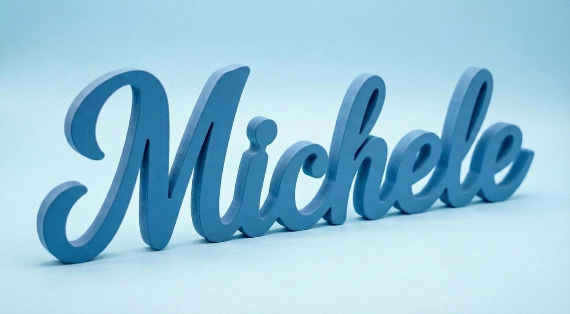 Scritta in legno azzurra personalizzata con il nome Michele, fotografata su sfondo azzurro soft.