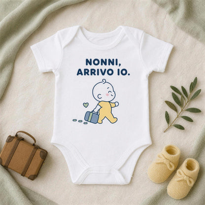 Body bianco con la frase «Nonni, arrivo io.» accanto a una valigetta in cuoio, scarpine gialle e un rametto d'ulivo