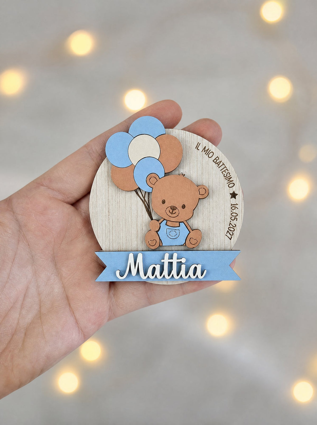 Calamita battesimo azzurra con il nome Mattia e la scritta Il mio Battesimo tenuta sul palmo di una mano