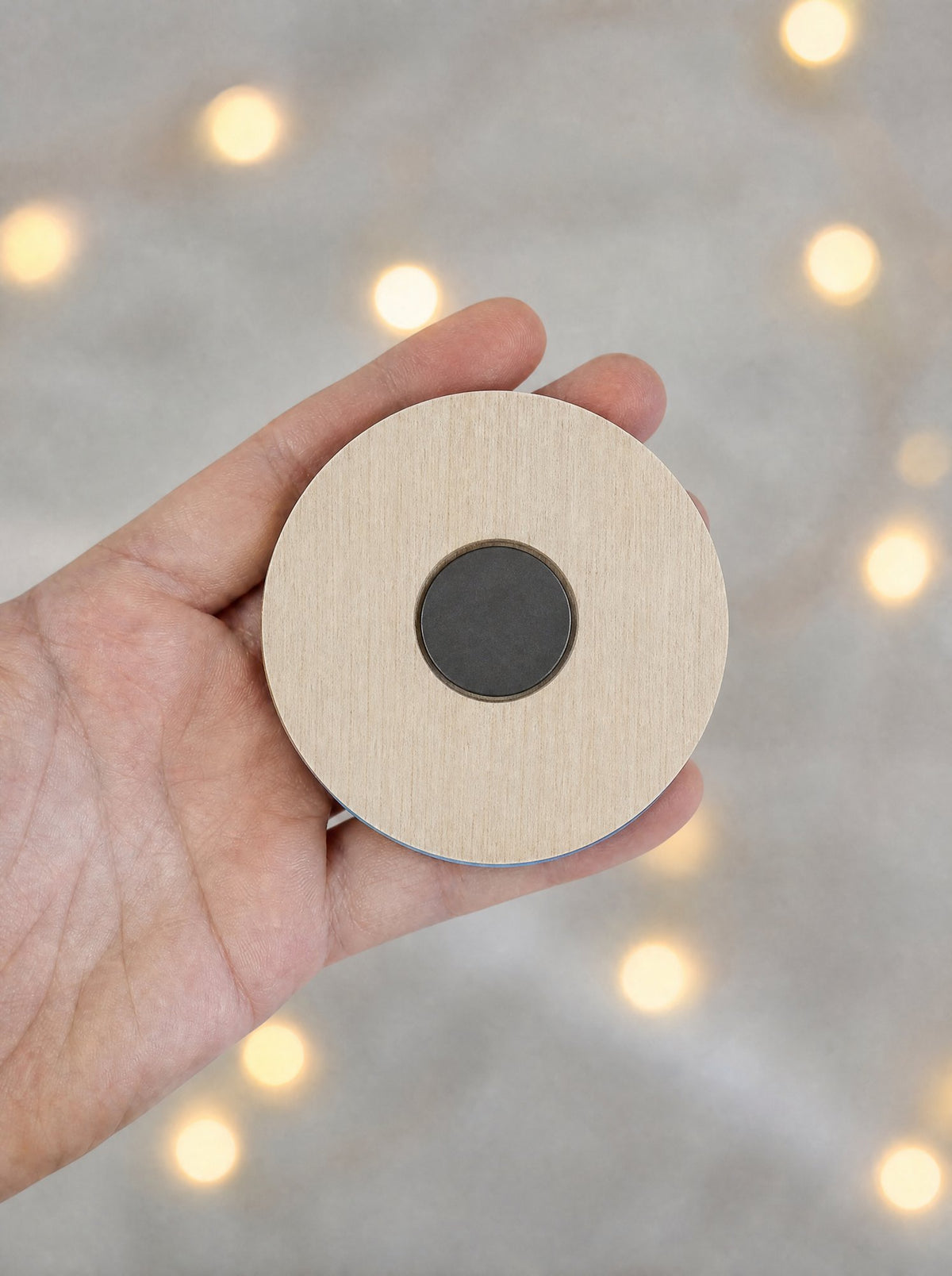 Retro della calamita: disco di legno chiaro con il magnete tondo incassato, tenuto in mano