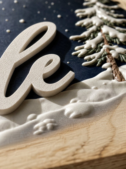 Dettaglio macro del nome in rilievo dal bordo netto, accanto alla texture morbida di neve e abete