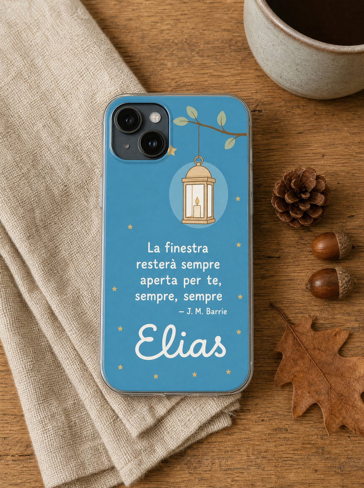 Cover per il papà con una lanterna accesa su un ramo, frase di J. M. Barrie e nome Elias, su un iPhone 15 visto dall'alto