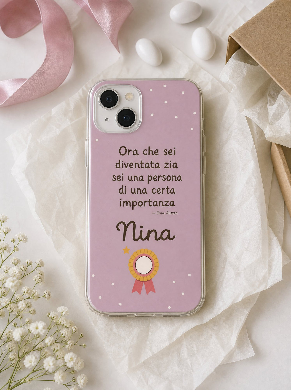 Cover per la zia con una coccarda, frase di Jane Austen e nome Nina, su un iPhone 15 visto dall'alto