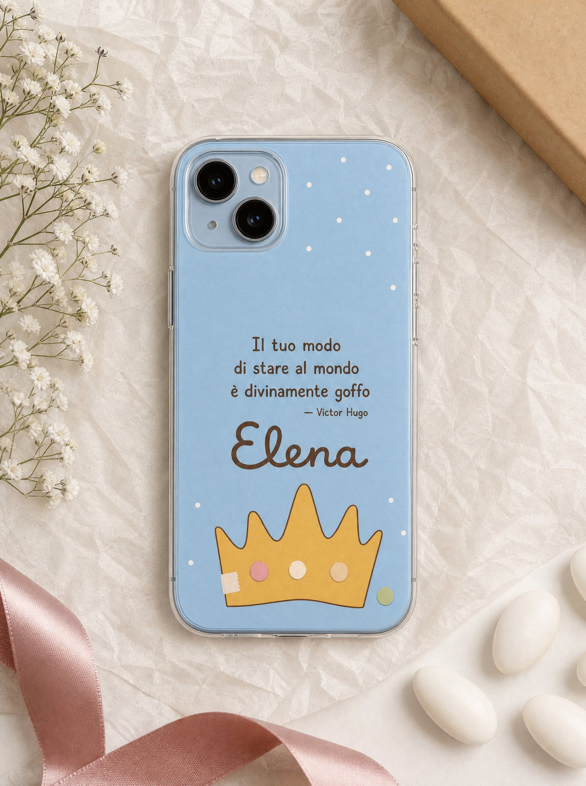 Cover per la zia e lo zio con una corona di carta, frase di Victor Hugo e nome Elena, su un iPhone 15 visto dall'alto