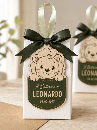 Scatolina battesimo con fiocco verde, tag a forma di leone davanti e una seconda scatolina sfocata dietro.