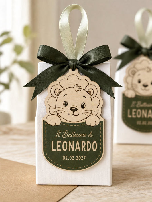 Scatolina battesimo con fiocco verde, tag a forma di leone davanti e una seconda scatolina sfocata dietro.